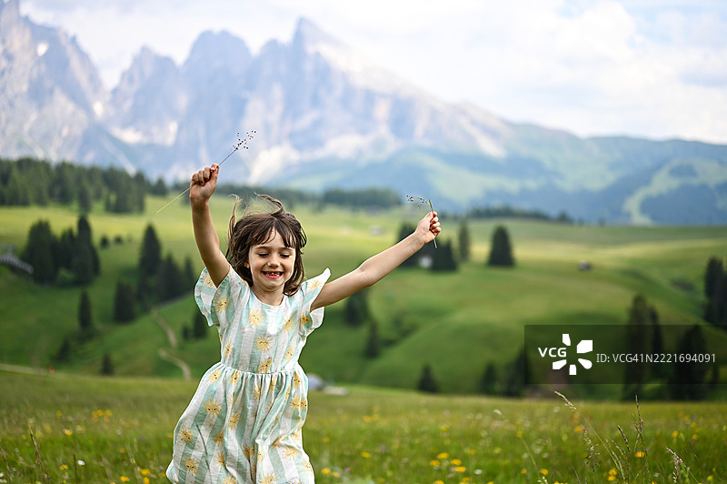 无忧无虑的女孩在草地上奔跑，背景是山脉。图片素材