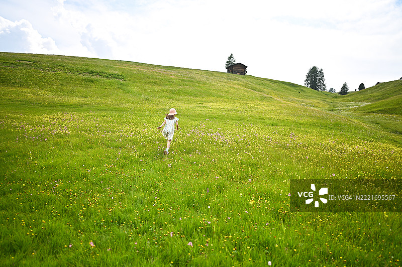 小女孩在意大利阿尔卑斯山的绿色山丘上奔向一座木屋图片素材