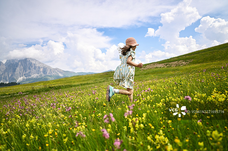 女孩在野花盛开的草地上奔跑，背景是山脉。图片素材