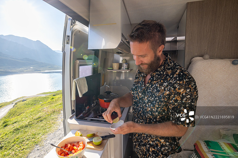 在露营车中准备餐点的男人，背景是壮丽的山景图片素材