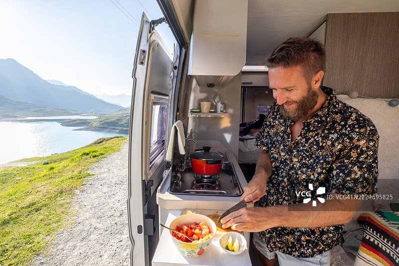 在露营车中准备餐点的男子，背景是壮丽的山景图片素材