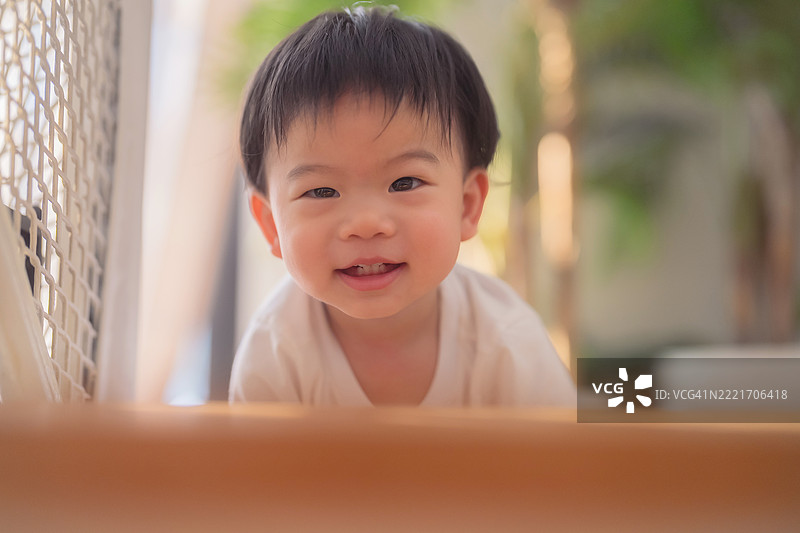 亚洲男婴快乐地在家中爬楼梯，带着好奇和活力微笑，探索客厅环境，展现早期儿童发展、积极的生活方式和有趣的学习时刻。图片素材