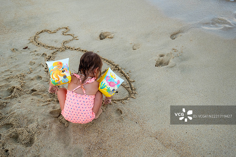 沙滩上的小女孩，坐在沙子上。图片素材