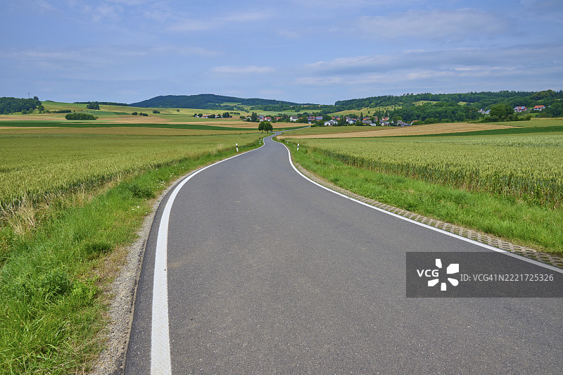 一条蜿蜒的乡村道路穿过丘陵、草地和小村庄的乡村风景，位于德国黑森州的巴德苏登-阿伦多夫镇，韦拉-迈斯纳县，欧洲。图片素材