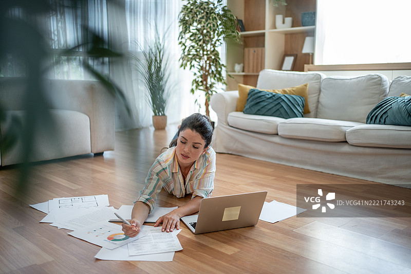 专注的年轻女性在家工作，分析图表和文件图片素材