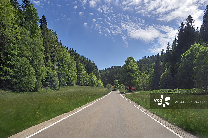 白云、春天的草地、乡村道路和位于德国巴伐利亚州阿尔戈伊地区的混合森林，靠近乌特库尔纳赫-维根斯巴赫图片素材