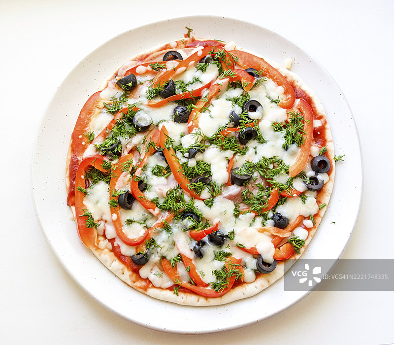 圆盘上的圆形披萨，上面有橄榄、辣椒、马苏里拉奶酪、莳萝和猪肉，俯视图图片素材
