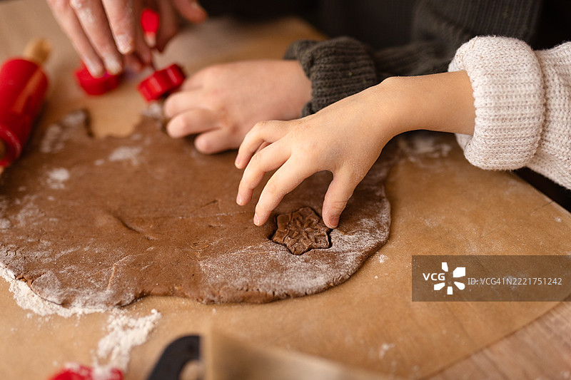 双手在木质表面上准备节日饼干，使用面团和切模。图片素材