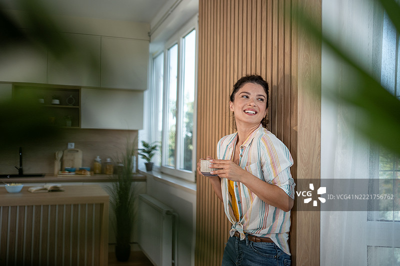 年轻女性在现代厨房中享受一杯咖啡图片素材