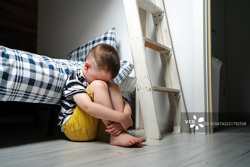 孤独悲伤的男孩独自坐在卧室床边的地板上图片素材
