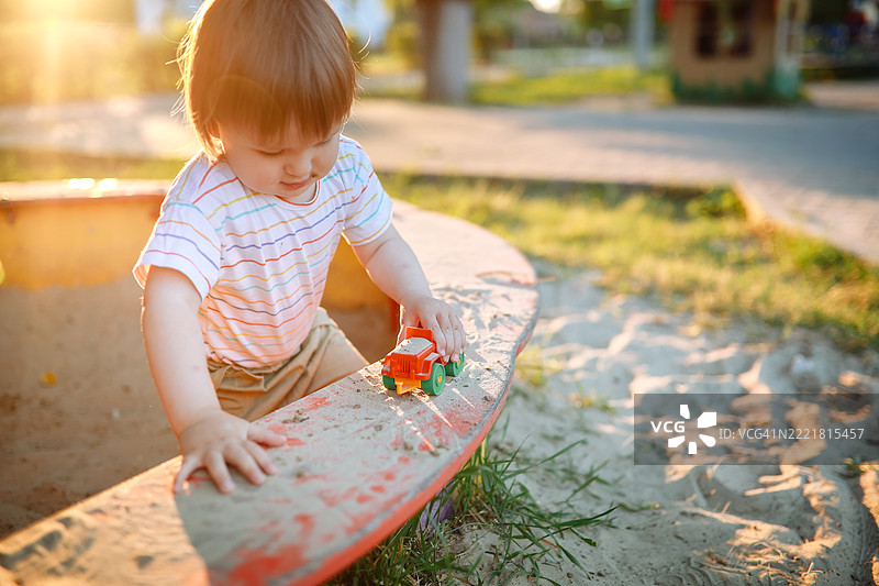 日落的温暖洒满沙箱：幼儿在玩玩具图片素材