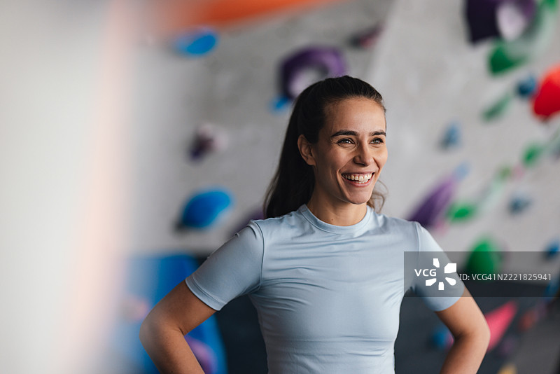 微笑的女性在室内攀岩馆，背景是五彩缤纷的攀岩点。图片素材