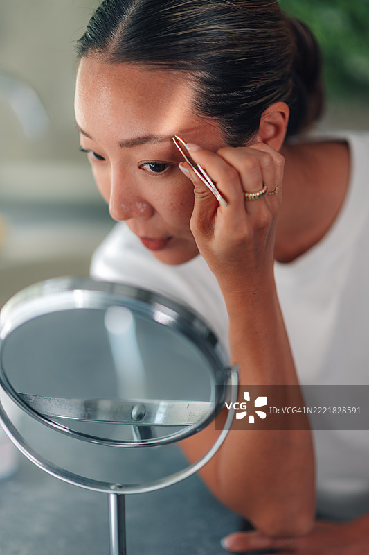 女人在浴室镜子前用镊子修眉图片素材