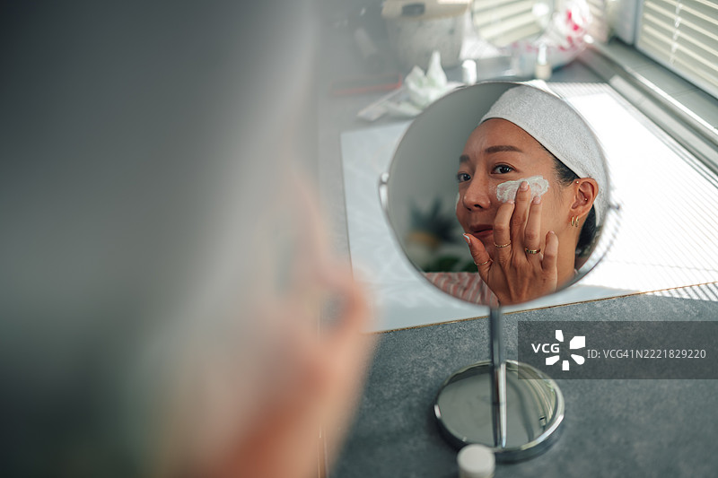 女人在家对着镜子涂抹面霜图片素材