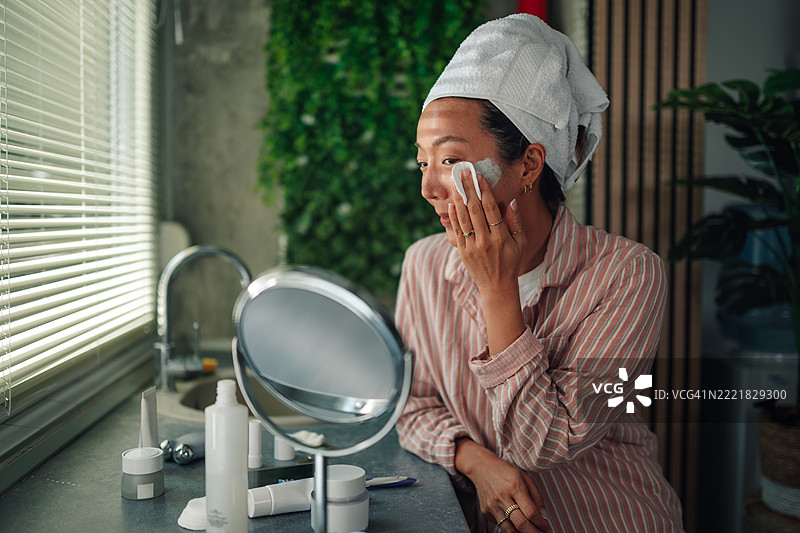 年轻的亚洲女性在现代浴室里用棉垫清洁面部图片素材