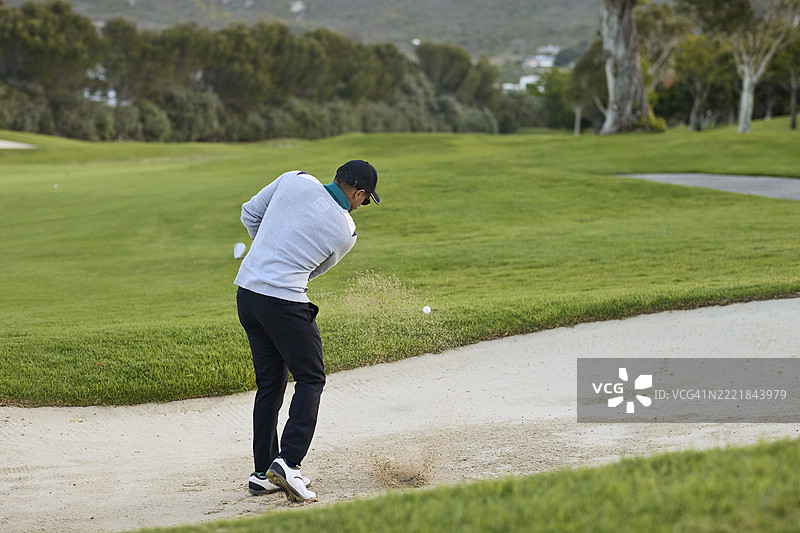 男子在沙坑中击打高尔夫球图片素材