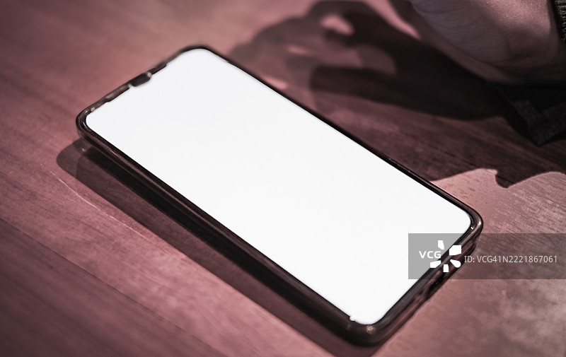 现代智能手机放置在木质表面或深色桌子上，屏幕为白色。图片素材