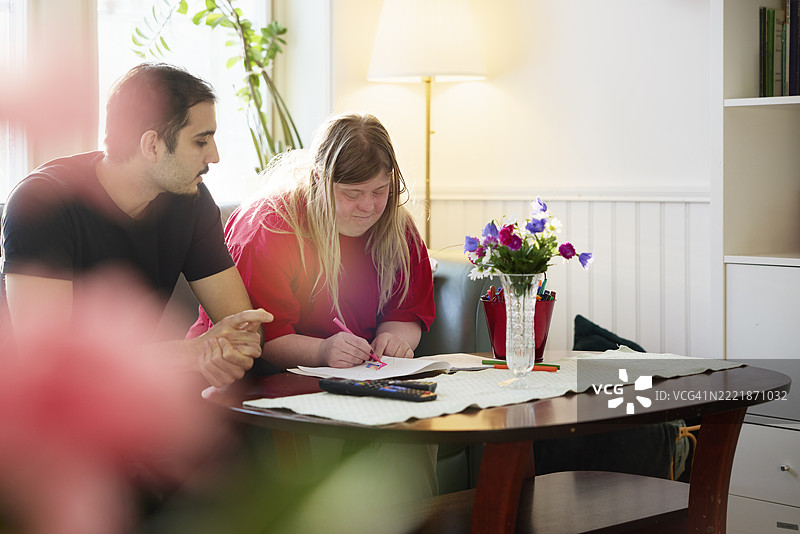 男护士与女性病人在养老院里坐着，一起在纸上涂色。图片素材