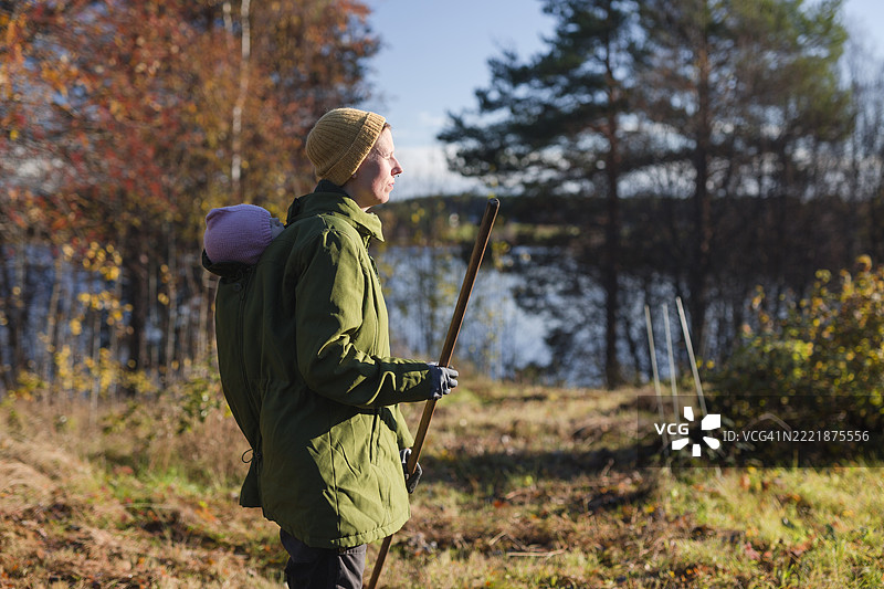 母亲背着婴儿，手持拐杖在森林中行走图片素材