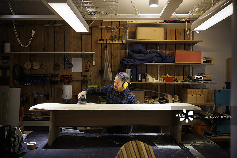 专注的男性木匠戴着降噪耳机在工作坊里打磨木材图片素材