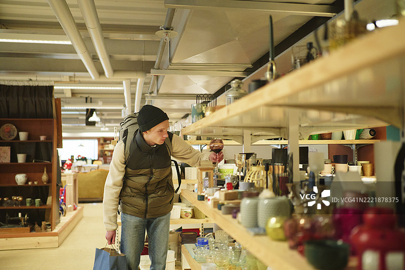 年轻男子在商店里从货架上挑选玻璃杯图片素材