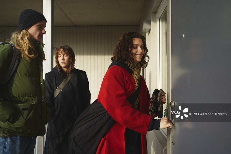 微笑的年轻女性与朋友们站在一起，关上汽车旅馆房间的门图片素材