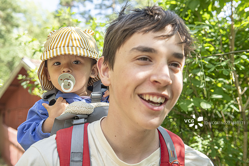 快乐的男孩在森林中背着弟弟徒步旅行图片素材