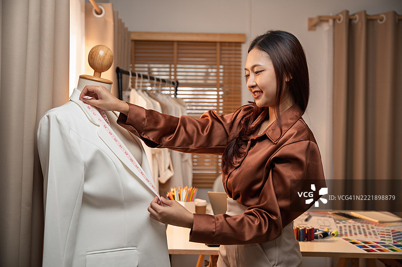 年轻的亚洲女性时装设计师在家工作。迷人的时尚美女正在创作新的服装系列。设计师和编辑们在她的工作室里设计服装。图片素材