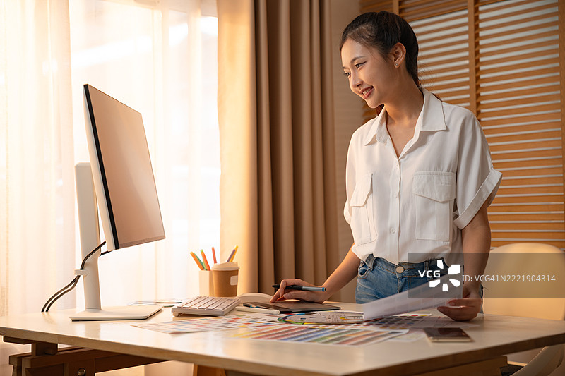 年轻的亚洲女性平面设计师在记录logo设计的笔记。色彩样本。艺术家在办公室的图形平板上绘制作品。平面设计师的创意编辑理念概念。图片素材
