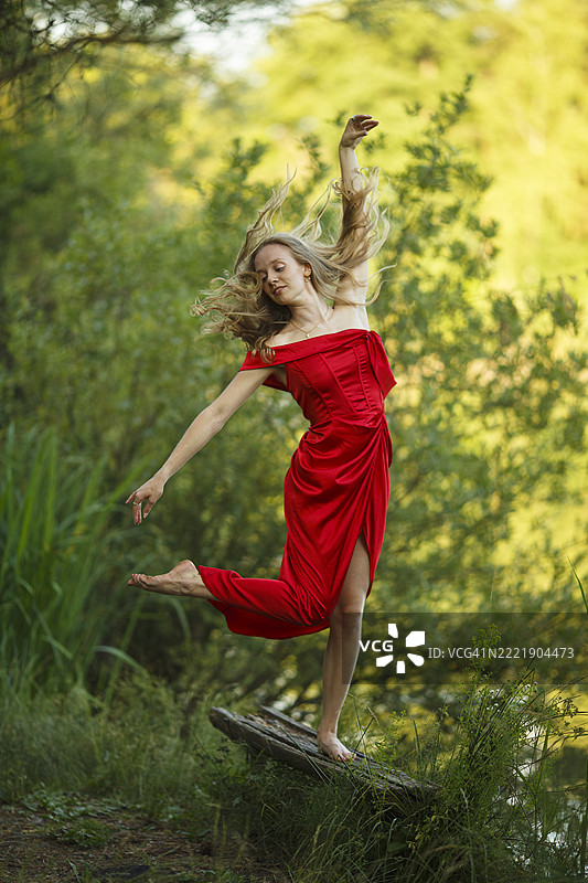 穿着红色裙子的女人在森林中表演现代舞，优雅的姿态融入自然。图片素材