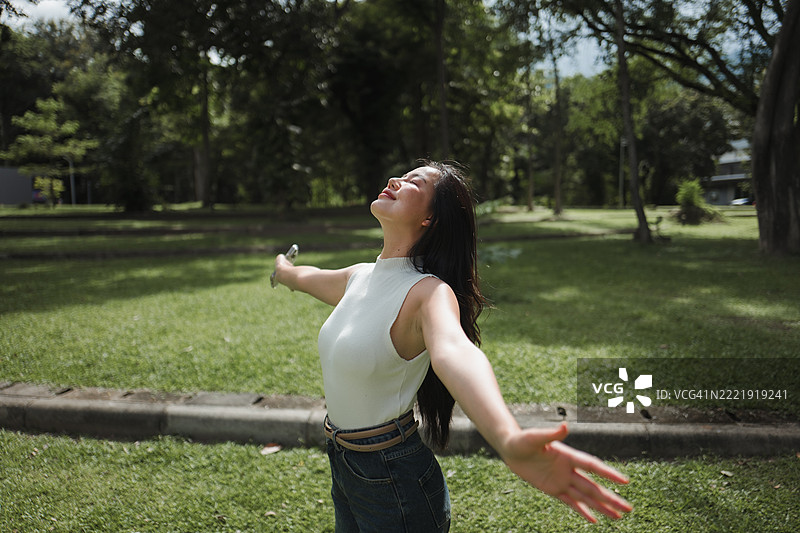 年轻女性在生机勃勃的绿色公园中张开双臂，享受新鲜空气，感受大自然的美丽，尽情拥抱自由。图片素材