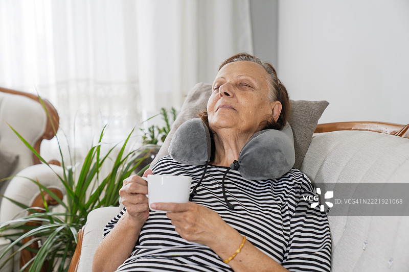 女人在家中放松，喝着绿茶。她坐在客厅的沙发上，享受饮品，面带微笑。图片素材