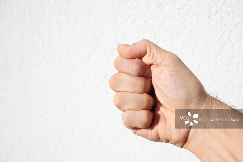 一个男人握紧的拳头，背景是白色墙壁。这个图像代表着力量、决心、内心的力量或情感的强度。图片素材