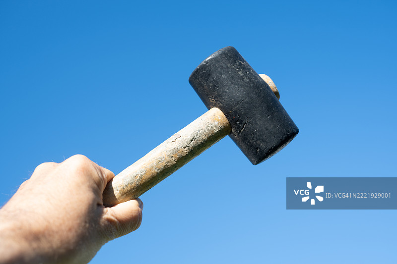 人手举着锤子，背景是晴朗的蓝天。图片素材