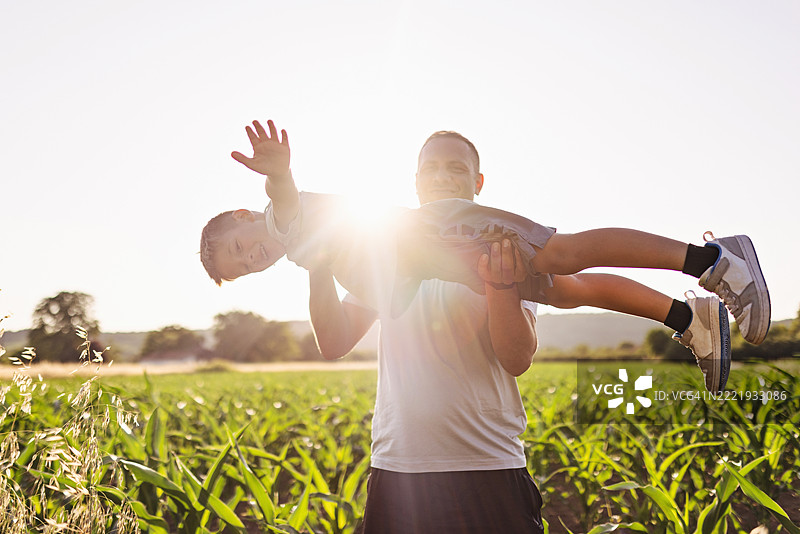 父亲在阳光明媚的田野中举起儿子，享受金色时光图片素材