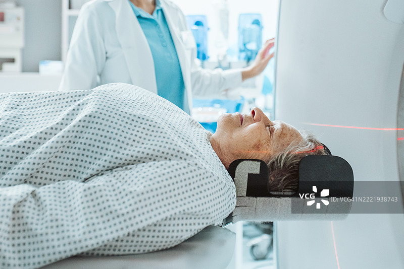 老年女性在CT扫描仪中准备进行头部扫描，激光对准。图片素材