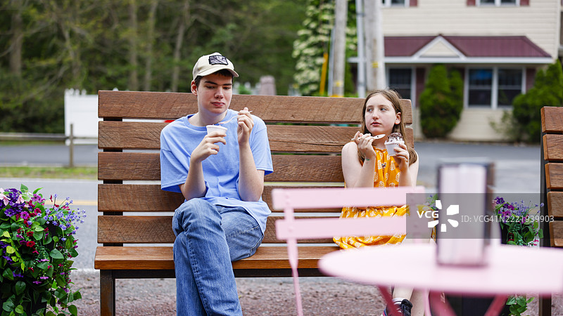 兄妹分享冰冻美食。自闭症青少年和青春期前的妹妹在公园长椅上吃冰淇淋。图片素材