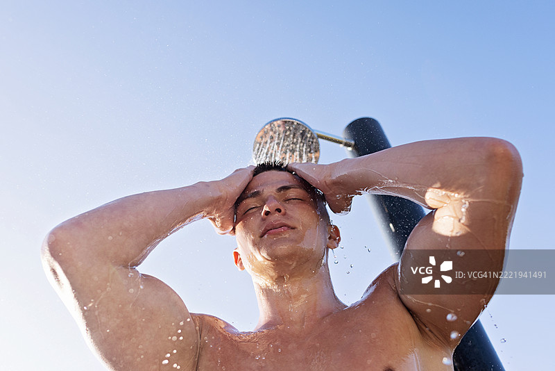 在清澈蓝天下，男子在户外淋浴中清新自己图片素材