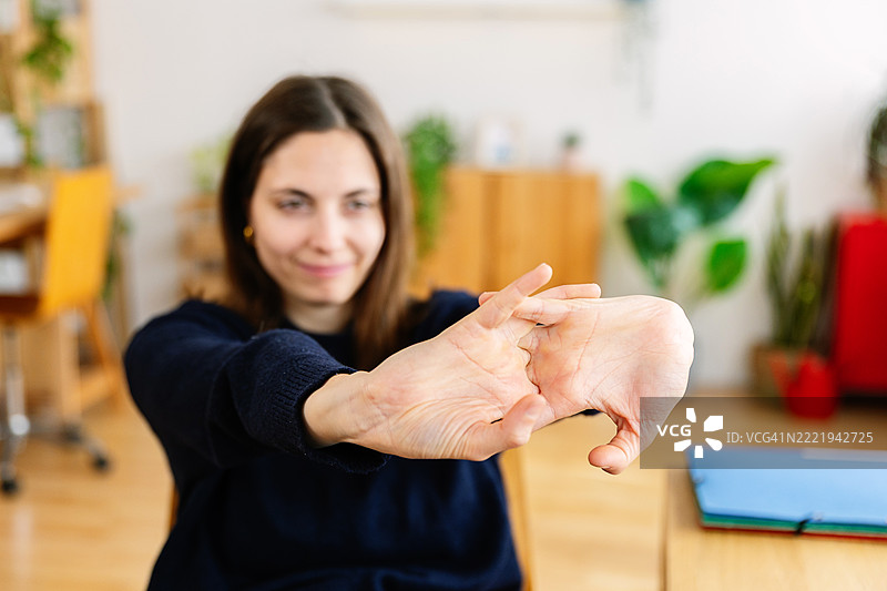 年轻女性在家办公桌前伸展手和手指图片素材