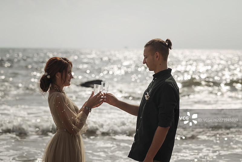 浪漫的新人情侣在海洋背景下举着香槟杯。图片素材