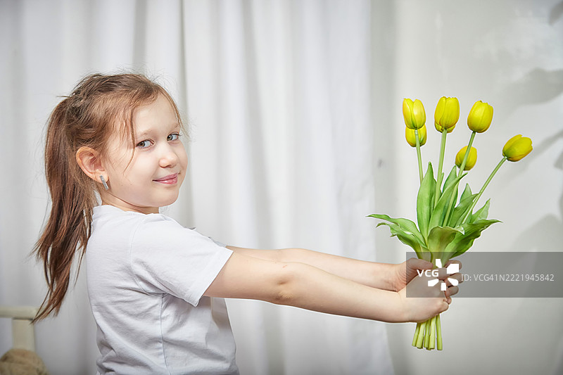 微笑的孩子在室内手捧一束黄色郁金香，光线明亮图片素材
