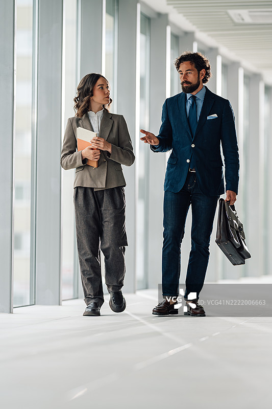 商务人士在现代办公室走廊中走动并交谈图片素材