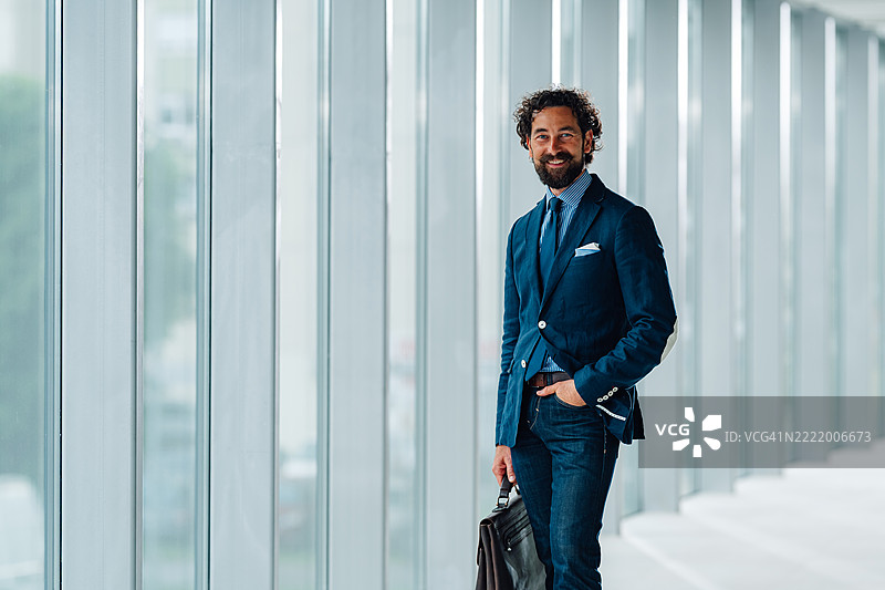 微笑的商人在现代办公大楼中手持公文包图片素材