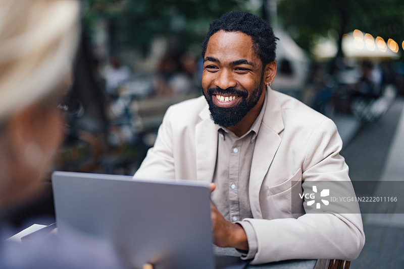 微笑的商人在城市环境中户外使用笔记本电脑工作图片素材