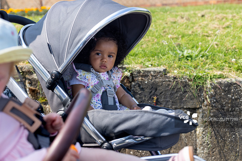 阳光明媚的日子里，困惑的婴儿坐在推车里图片素材