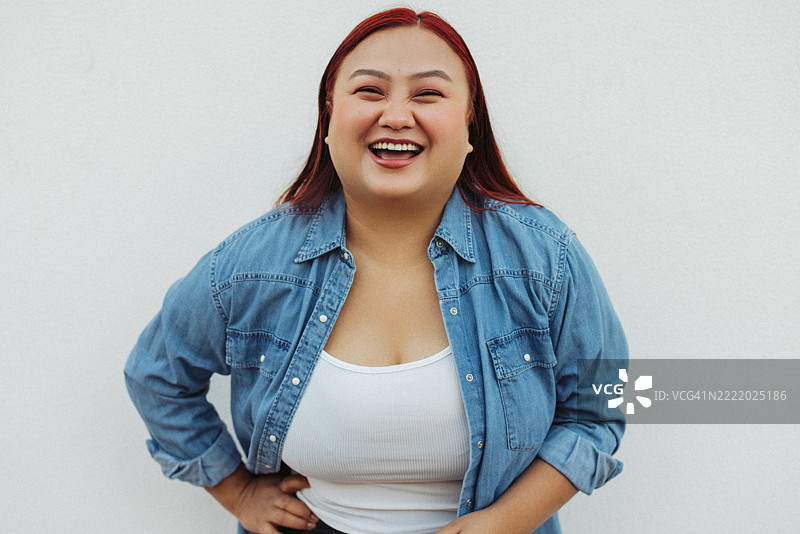 自信的女性穿着休闲牛仔夹克，微笑着站在纯白色墙壁前图片素材