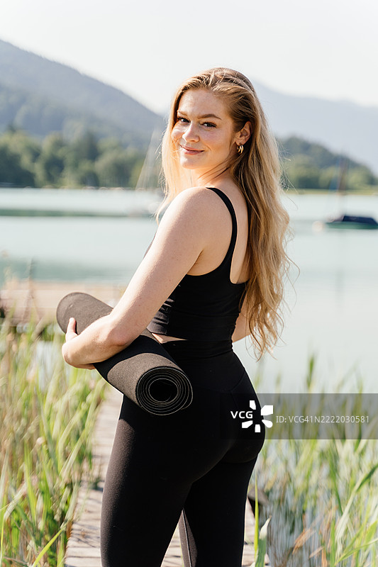 穿着瑜伽服的女性在码头上走着，手里拿着瑜伽垫，准备进行瑜伽练习。图片素材