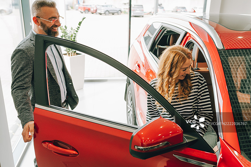 汽车销售员在汽车展厅向女性顾客展示一款新跑车图片素材