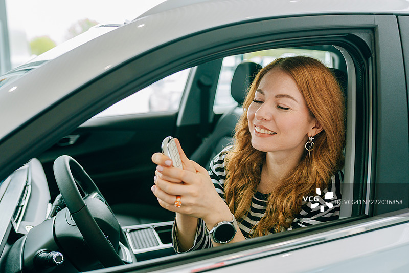 购车。快乐的女性司机在车内微笑着握着新车钥匙，身处于汽车经销商处。图片素材