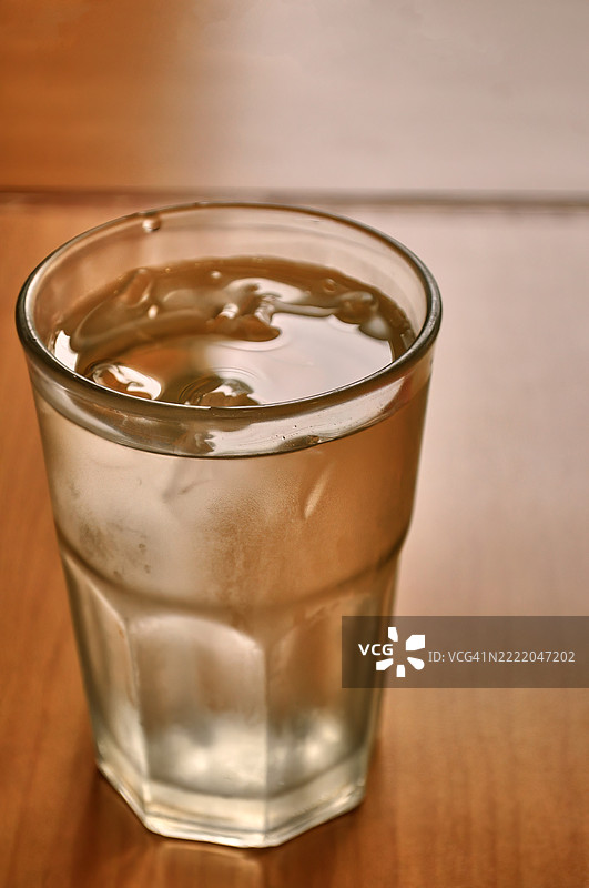 一杯冰块水放在木质表面上。图片素材